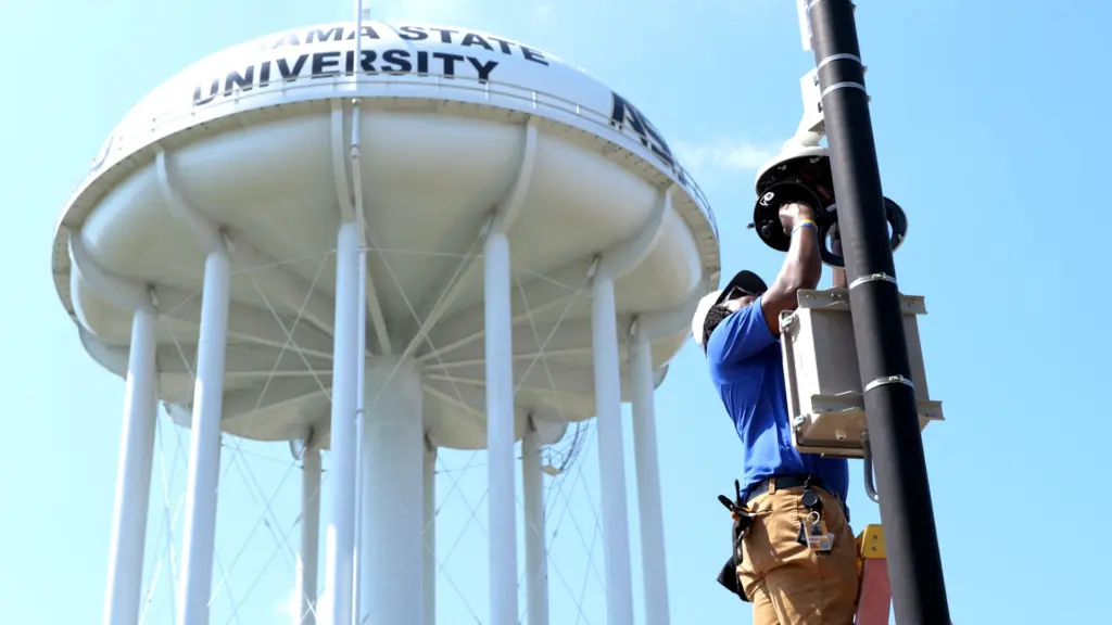 C2 Technology Group technician servicing pole-mounted equipment beside the Alabama State University water tower